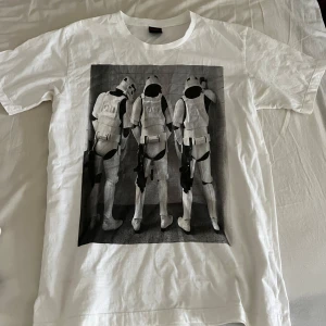 Vit t-shirt med Stormtrooper-tryck - Säljer en vit t-shirt med ett coolt Stormtrooper-tryck på framsidan. Perfekt för alla Star Wars-fans! T-shirten är kortärmad och gjord i mjukt bomullsmaterial.