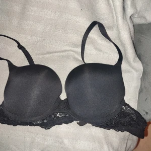 Svart bh push up - Snygg svart bh med vadderade kupor och spetsdetaljer längs kanten. Justerbara axelband för perfekt passform. Perfekt för att ge stöd och komfort hela dagen.