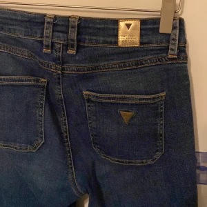 Blå jeans från Guess - Snygga blå jeans från Guess med klassisk femficksdesign och en diskret logga på bakfickan.  Fint skick! Storlek W25