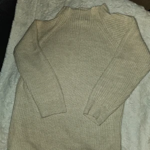Beige stickad tröja -  Nytt Säljer en supermysig beige stickad tröja. Den har halvpolo och långa ärmar, perfekt för kyliga dagar. Tröjan är ribbad vilket ger den en snygg textur och extra värme.  Den är stor i strl och mer som M. Kan användas som kort klänning