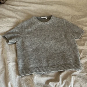 Stickad tröja från Zara - Säljer denna grå stickade tröja från Zara. Den är kortärmad och har en ribbad kant vid ärmslut och nederkant. Använd 5 gånger, och inte mkt tvättad💞