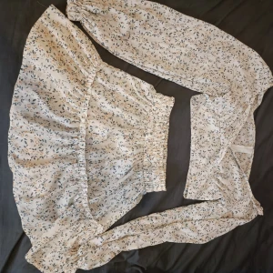 Blommig offshoulder topp - Säljer en superfin blommig topp med långa ärmar och en kjol som har en elastisk midja. Toppen är i ett lätt och luftigt material 🤍 obs betalning sker via swish 