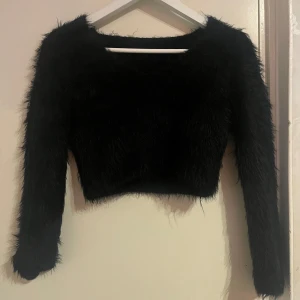 Svart fluffig tröja - Säljer en svart fluffig tröja med lång ärm och croppad passform. Perfekt för att ge en trendig touch till din outfit. Tröjan är mysig och stilren, idealisk för kyligare dagar.
