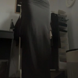 Svart långkjol - Snygg svart långkjol med en tight passform. Kjolen har en slits som ger en elegant touch och gör den perfekt för olika tillfällen. Den är enkel och stilren, vilket gör den lätt att matcha med olika toppar och accessoarer.