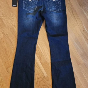 Low waist true religion jeans bootcut  - Snygga mörkblå bootcut jeans med knappar fram. De har en klassisk femficksdesign och en stilren tvätt som ger en cool look. Perfekta för dig som gillar en tidlös stil med en modern twist. Pris kan diskuteras.