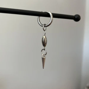 Silverfärgat örhänge i rostfritt stål  - Stilrent silverfärgat örhänge med en rund ring och hängande nit. Perfekt för att ge en edgy touch till din stil. Lätt att matcha med andra smycken.