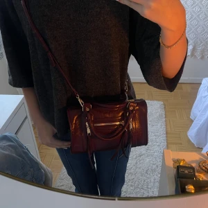 Vinröd väska  - En glasig vindröd väska med fransar på dragkedjorna framtill med gulddetaljer💕Använd på gånger💗 