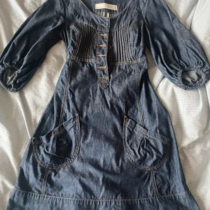 Blå jeansklänning från Sub Culture - Snygg vintage blå jeansklänning från Sub Culture med knappar framtill och puffiga trekvartsärmar. Klänningen har dekorativa sömmar och praktiska fickor. Perfekt för en avslappnad stil med en touch av vintage. 