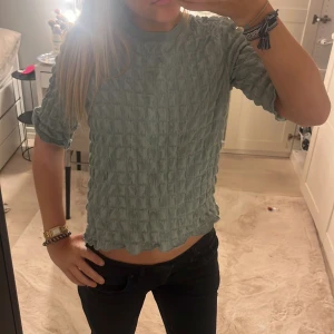 Grön topp från Monki - Säljer en grön topp från Monki i ett unikt texturerat material. Toppen har korta ärmar och en croppad passform som ger en trendig look. Perfekt för att lägga till lite stil i din garderob.