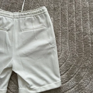 Vita shorts med snörning - Snygga vita shorts med elastisk midja och snörning för en bekväm passform. De har fickor på sidorna och uppvikta benslut för en stilren look. Perfekta för varma dagar.
