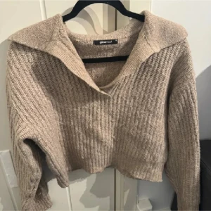 Beige stickad tröja från Gina Tricot - Säljer en mysig beige stickad tröja från Gina Tricot. Tröjan har en bred krage och är croppad med långa ärmar. Perfekt för kyliga dagar!