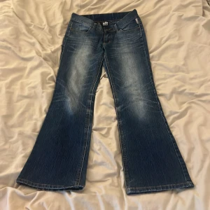 Blå bootcut jeans från Lab Industries - Snygga blå bootcut jeans från Lab Industries med klassisk femficksdesign och knappgylf. Jeansen har en lätt tvättad look och är perfekta för en avslappnad stil. De har en normal passform och är tillverkade i jeansmaterial.