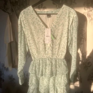 Blommig klänning med volangdetaljer - Charmig blommig klänning i ljusgrönt/turkost med volangdetaljer och v-ringning. Klänningen har långa ärmar och en luftig passform, perfekt för vår och sommar. Tillverkad i ett lätt och bekvämt material. 🩵Helt oanvänd då den var för liten när jag fick den, lapp sitter kvar! Pris kan diskuteras 💓