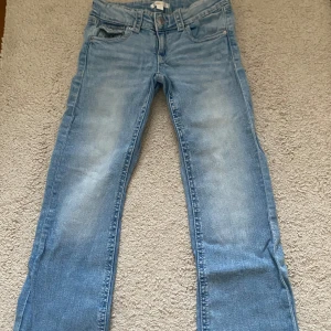Ljusblå lågmidjade bootcut jeans från Gina Tricot - Snygga ljusblå jeans från Gina Tricot i storlek 158. De har en klassisk femficksdesign och en knappgylf. Perfekta för en avslappnad stil.