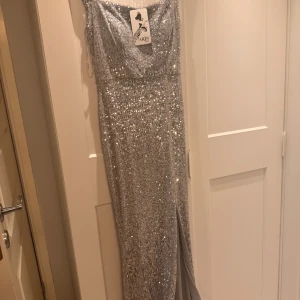 En jätte fin glittrig festklänning med slips - Snygg och elegant långklänning i silver från Arni. Klänningen är glittrig och har en slits framtill som ger en extra touch. Perfekt för festliga tillfällen. Klänningen är aldrig använd ( prislapp sitter kvar ). Priset är inte hugget i sten! Hör av er om ni undrar över något 😊