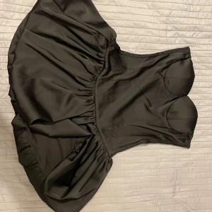 Svart klänning med volangdetaljer - Snygg svart klänning med volangdetaljer och en tight passform upptill. Klänningen har en kort längd och är perfekt för en festlig kväll. Materialet ger en elegant look och den smockade ryggen ger extra komfort.