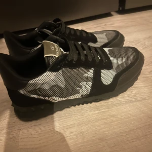 Valentino Rockrunner svart vit - Snygga Valentino Rockrunner sneakers i svart och grått med ett coolt camouflage-mönster. Skorna har en klassisk snörning och en robust sula som ger bra grepp. Perfekta för att ge din outfit en stilfull touch.
