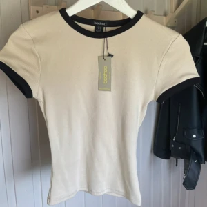 Beige ribbad t-shirt från Boohoo - Snygg beige ribbad t-shirt från Boohoo med kontrasterande svarta kanter vid hals och ärmar. Helt ny