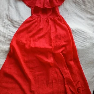 Härligt röd offshoulder klänning med slits - Klänningen har åtsittande liv och  en luftig kjol med flow och är perfekt för sommarens alla tillfällen. Den är tillverkad i ett lätt och bekvämt material som ger en fin rörelse och är luftigt och svalt om det är varmt 