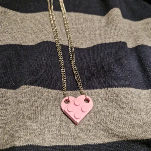 Rosa hjärthalsband med lego - Två halsband med varsinn legobit som tillsammans formar ett hjärta. Kedjorna är tunna och silverfärgade. Perfekt för att dela med en vän eller partner.