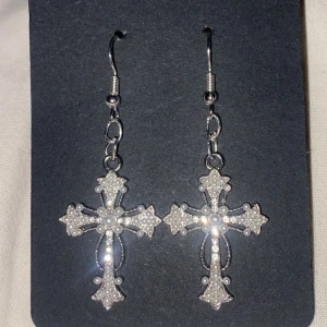 Silvriga korsformade örhängen - Egengjorda silvriga örhängen i form av kors med glittriga detaljer. Perfekta för att ge en elegant touch till din outfit. De hänger från en enkel krok och har en fin detaljrikedom.