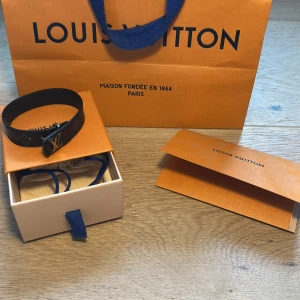 Svart armband från Louis Vuitton - Ett ÄKTA svart armband från Louis Vuitton i läder med märkets ikoniska LV-logotyp i metall. originalförpackning och kvitto kommer med armbandet. Tveka inte att skriva för mer frågor