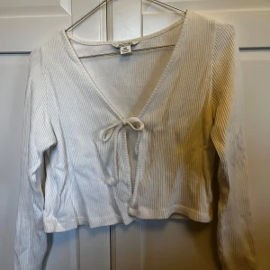 Vit ribbad kofta med knytning - Säljer en vit ribbad kofta från monki med knytning framtill. Den har en v-ringad design och långa ärmar.