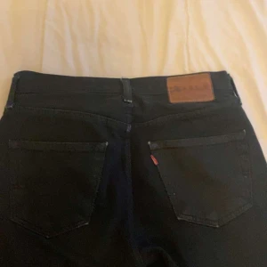 Svarta jeans från Levi's - Snygga svarta jeans från Levi's med klassisk design. De har en rak passform och är tillverkade i slitstarkt denim. Perfekta för en stilren look. Märkeslappen i läder baktill ger en autentisk touch.