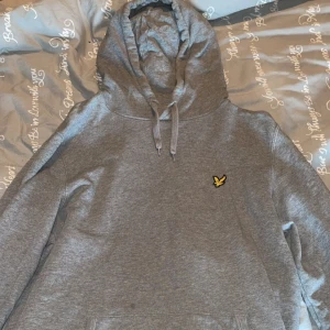 Grå hoodie från Lyle & Scott - Säljer en stilren grå hoodie från Lyle & Scott med deras ikoniska gula logga på bröstet. I storlek L