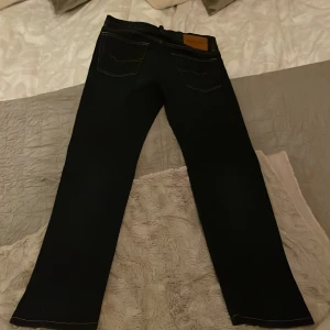 Mörkblå jeans från Diesel - Säljer ett par mörkblå jeans från Diesel, modell D-Mihtry. De har en straight passform och är tillverkade i stretchmaterial för extra komfort. Klassisk design med fem fickor och en snygg läderdetalj med Diesel-logga på baksidan. 