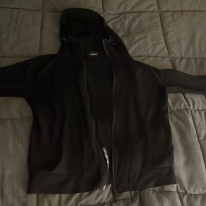 Svart huvtröja från Emporio Armani - Säljer en stilren svart huvtröja från Emporio Armani med dragkedja framtill. Tröjan har en luva och ribbade muddar vid ärmslut och nederkant. Perfekt för en casual look.