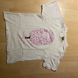 Vit t-shirt från Bape - Säljer en vit t-shirt från Bape med ett unikt tryck i rosa och lila på framsidan. T-shirten har korta ärmar och är gjord i bomull. Perfekt för dig som gillar streetwear och vill ha något som sticker ut. 🌸