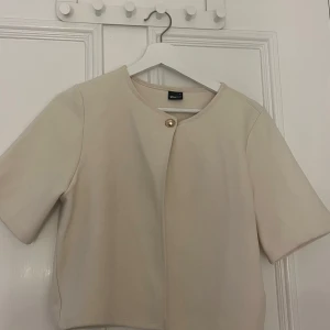Beige kofta från Gina Tricot - Säljer en kortärmad kofta i lite tjockare tyg som är från Gina Tricot. Koftan är beige och i storlek M. Den passar mig som vanligt vis är en storlek S. Jättefin🩷Knappen är lite lös, då den var så när jag köpte den, men det borde gå att fixa genom att sy