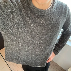 Grå stickad tröja - Säljer en mysig grå stickad tröja med rund hals. Perfekt för kyliga dagar och enkel att matcha med olika outfits. Tröjan har långa ärmar och en bekväm passform.
