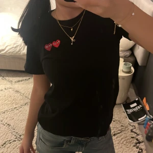 Svart t-shirt med hjärtdetalj - Säljer en svart t-shirt med korta ärmar och en cool hjärtdetalj i rött på bröstet. Perfekt för en avslappnad stil. Passar bra till jeans eller kjol.