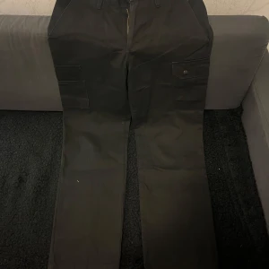 Svarta cargopants med fickor - Snygga svarta cargopants med flera praktiska fickor och dragkedja. Perfekta för en avslappnad stil och passar till många olika outfits. Byxorna har en normal passform och är tillverkade i ett slitstarkt material.