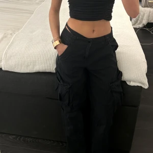 Svarta cargobyxor - Snygga svarta cargobyxor med flera fickor och en avslappnad passform. Perfekta för en cool och avslappnad stil. Byxorna har en midwaist design och är gjorda i ett slitstarkt material.