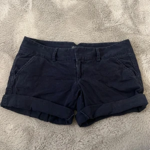 Mörkblå lågmidjade shorts från American Eagle Outfitters - Snygga mörkblå shorts från American Eagle Outfitters med stretch för extra komfort. De har en klassisk design med fickor fram och bak samt hällor för bälte. Perfekta för en avslappnad stil. Det står inte vilken storlek det är men skulle gissa på strl 38! Skriv för mått eller fler bilder!! 💙