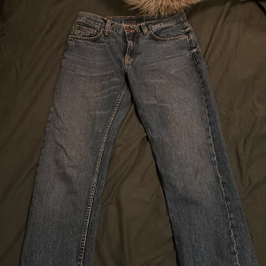 Mörkblå jeans från Nudie Jeans - Säljer ett par mörkblå jeans från Nudie Jeans med klassisk femficksdesign och orange sömmar. Jeansen har en rak passform och är tillverkade i slitstarkt denim. Perfekta för en avslappnad stil. Använda 2ggr