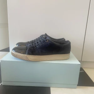 Lanvin - Snygga sneakers från Lanvin med en stilren design. Skorna har en glansig tå och snörning framtill. Perfekta för en trendig look. Skick 7,5/10 (finns en liten defekt syns på sista bilden)