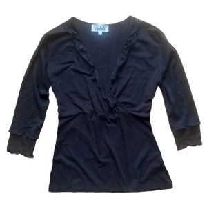 Svart omlottopp från Isolde - Snygg svart omlottopp från Isolde med trekvartsärmar och volangdetaljer längs halsringningen. Strl L på lapp men mer en S/M i storlek. 