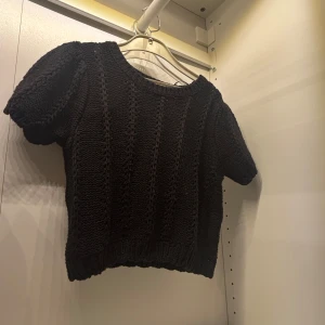 Svart stickad tröja - Säljer en svart stickad tröja med korta ärmar. Tröjan har ett fint stickat mönster och ribbade kanter. Perfekt för en stilren look.