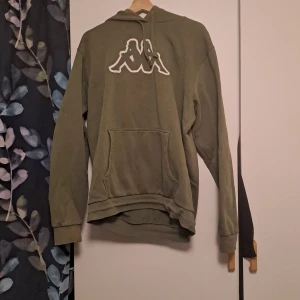 Grön hoodie från Kappa - Säljer en grön hoodie från Kappa med det klassiska logotypen på bröstet. Väl amvänd men märks inget på själva hoodien förutom på snörena. Liten i stolek kan jag tycka