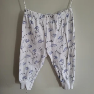 Vita byxor med truckmönster - Söta vita byxor med blått truckmönster. Perfekta för barn som älskar fordon! Byxorna har resår i midjan och muddar vid bensluten för extra komfort. Storlek 68!