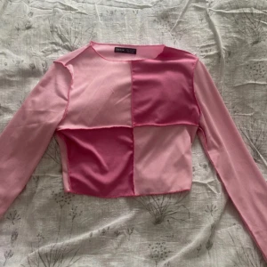 Rosa långärmad topp från Shein - Säljer en rosa långärmad topp från Shein med ett coolt blockmönster i olika nyanser av rosa. Toppen är croppad och har en tight passform, perfekt för en trendig look.