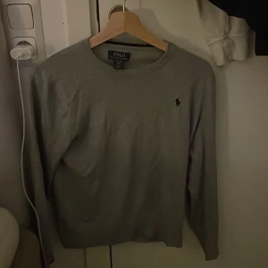 Grå tröja från Polo Ralph Lauren - Säljer en stilren grå tröja från Polo Ralph Lauren med rund halsringning och det klassiska logotypbroderiet på bröstet. Tröjan har långa ärmar och är perfekt för en avslappnad men ändå elegant look.
