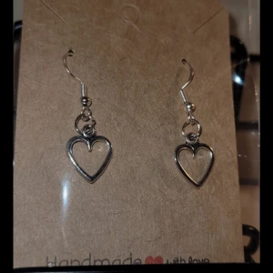 Silverfärgade hjärtformade örhängen - Säljer ett par handgjorda silverfärgade örhängen med hjärtformad design. De är enkla men stilrena och passar perfekt för att ge en romantisk touch till din outfit. Perfekta för alla tillfällen där du vill sprida lite kärlek.❤️
