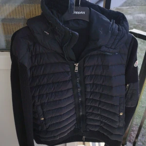 Moncler cardigan  - Snygg svart Moncler cardigan jacka med luva. Använd ett par gånger men inga täcken på användning ser ut som helt nu. Storlek L.                    Den har stått hemma och samlat på sig lite dam och sälj där av till ett billigt pris 