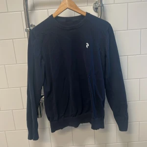 Mörkblå tröja med logotyp - Säljer en stilren mörkblå tröja med en liten vit logotyp på bröstet. Knappast använd med bra skick. Försöker frakta samma dag 