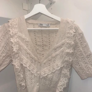 Beige kofta -  Elegant beige kofta från Zara med vackra spetsdetaljer längs halsringningen och framsidan. Koftan har en v-ringad design och knappar framtill. Aldrig använd🌟
